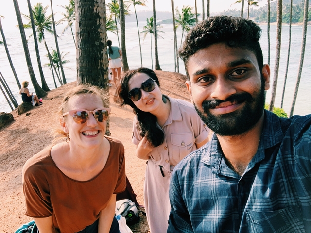 Three people taking a selfie on a cliffside overlooking the ocean.