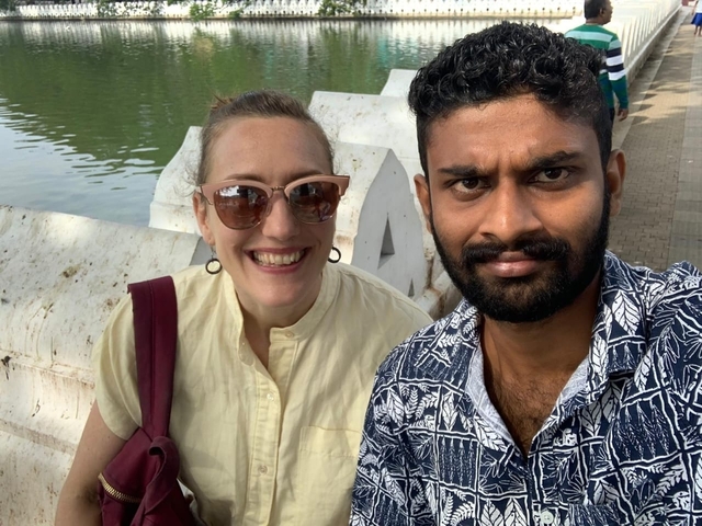 Two people taking a selfie near a water body and bridge.