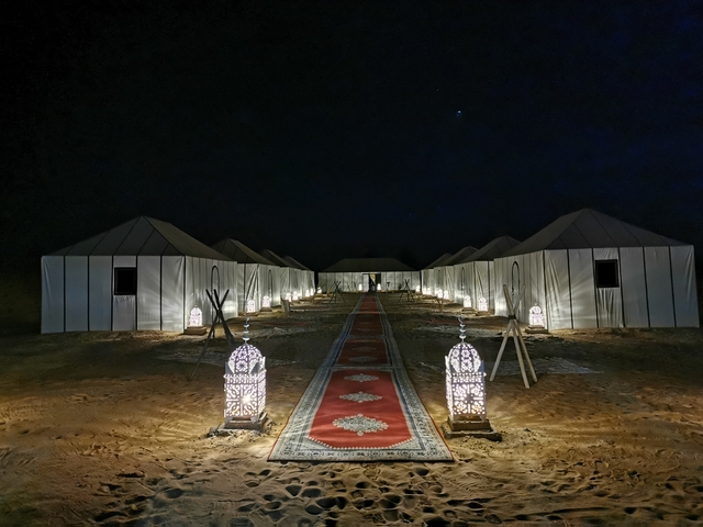       Elegant desert camp with tents and lanterns illuminated at night.
  