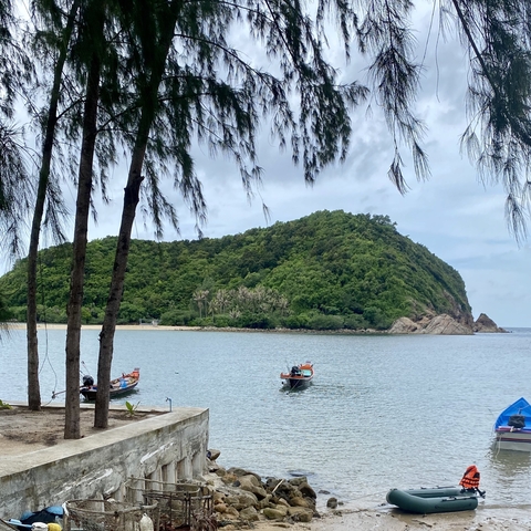       Boats near a mountain and beach under a cloudy sky.
  