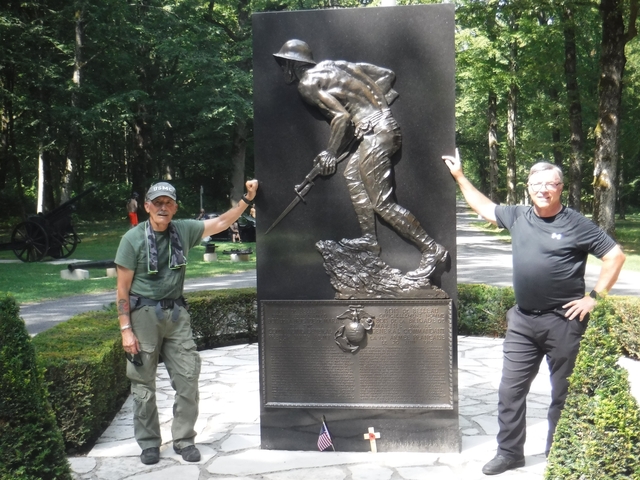       Two people posing with a statue in a wooded area.
  