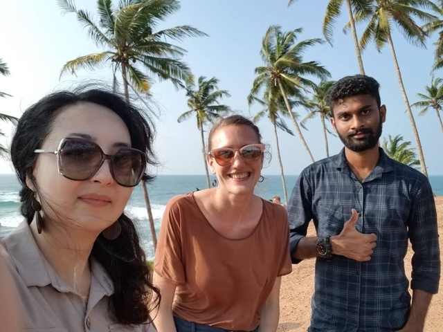 Three people posing with a scenic palm beach in the background.