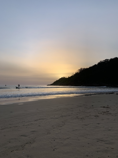 Surfer on a calm ocean at sunrise with a sandy beach.