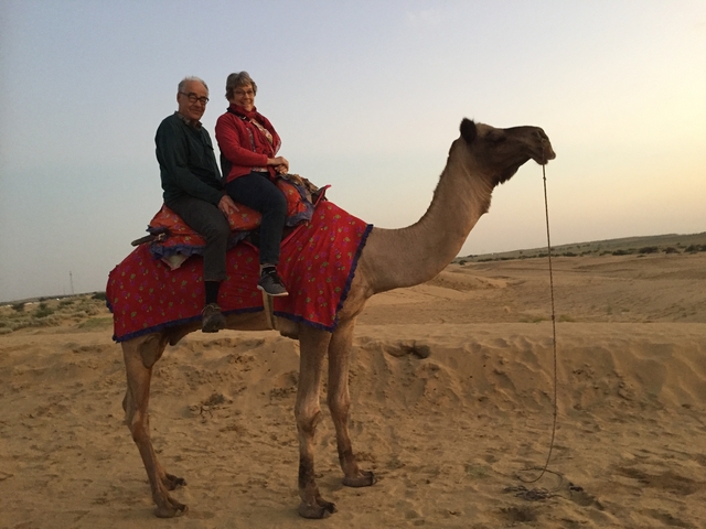 Couple riding a camel in a desert landscape.