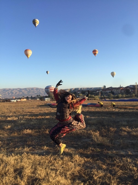       Woman jumping with hot air balloons in the background at sunrise.
  