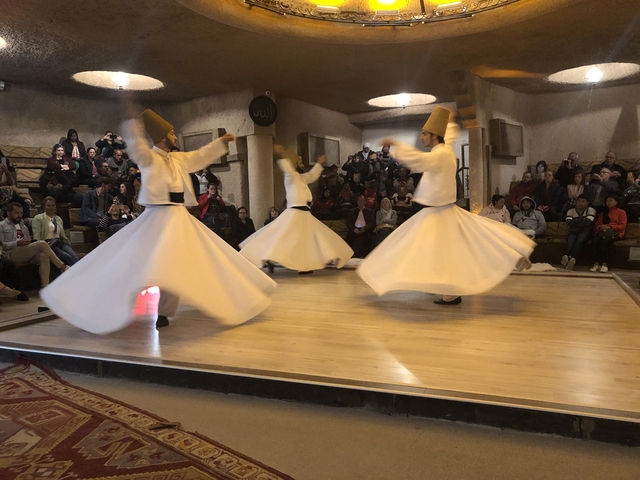       Dancers performing whirling dervish dance inside a hall.
  