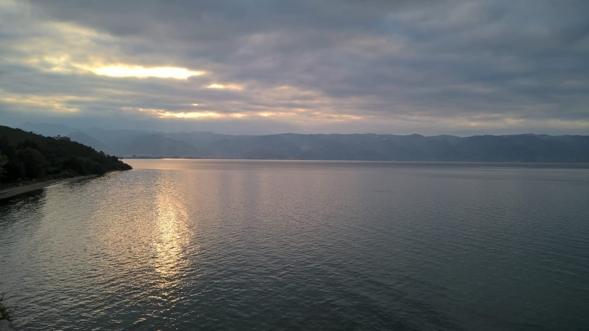 Wide view of a lake at sunset with mountains in the background.