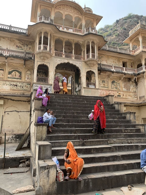       People on steps of a historic building with frescoes.
  