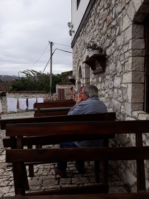 Older man sitting on wooden bench by stone wall