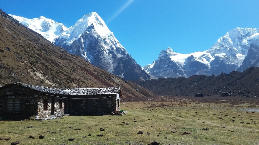 Small stone house in a valley surrounded by snow-capped mountains.