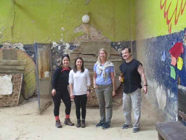 Four people standing indoors with rustic walls.