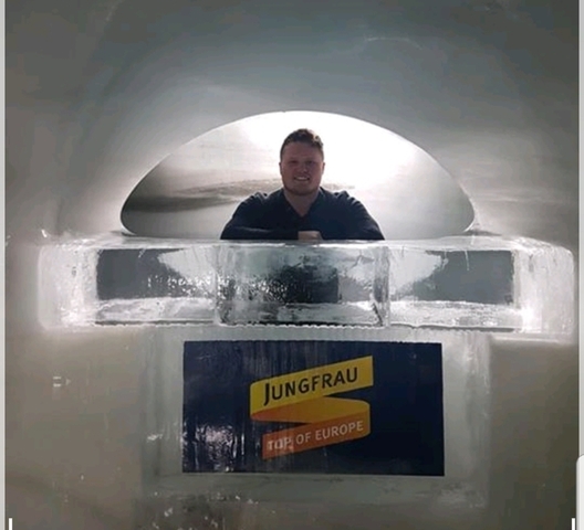 A person posing with an ice sculpture inside an ice cave.
