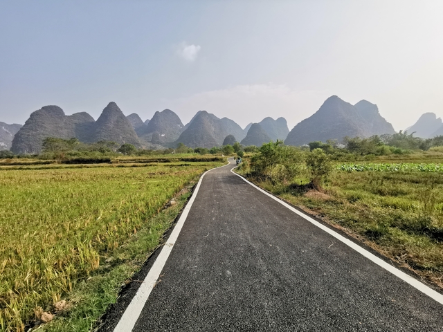       A road leading to pointed karst mountains in a rural landscape.
  