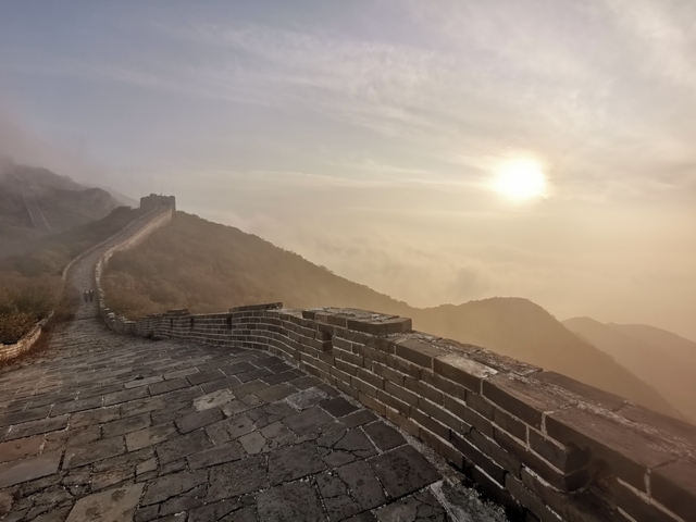 Misty view of a stone wall extending over hills with morning sun.