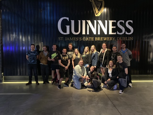 Group of people posing in front of Guinness brewery sign.