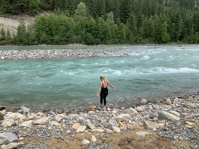 Person stepping into a river surrounded by rocks and trees.