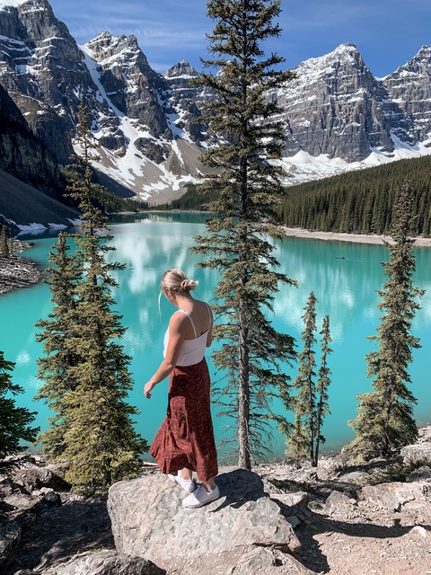 Woman overlooking a turquoise lake with surrounding forest and mountains.