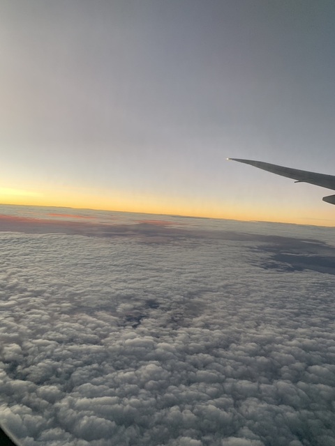 View from an airplane window over clouds at sunset.