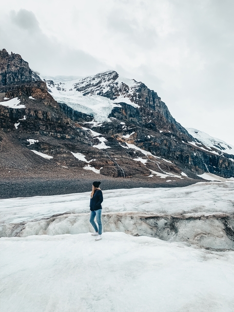 Person standing on a snowy mountain with rugged cliffs and ice in the background.