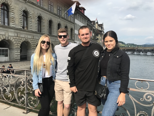       Group photo on a bridge over a lake with mountains.
  