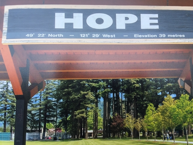 Sign indicating geographic coordinates with trees in the background.