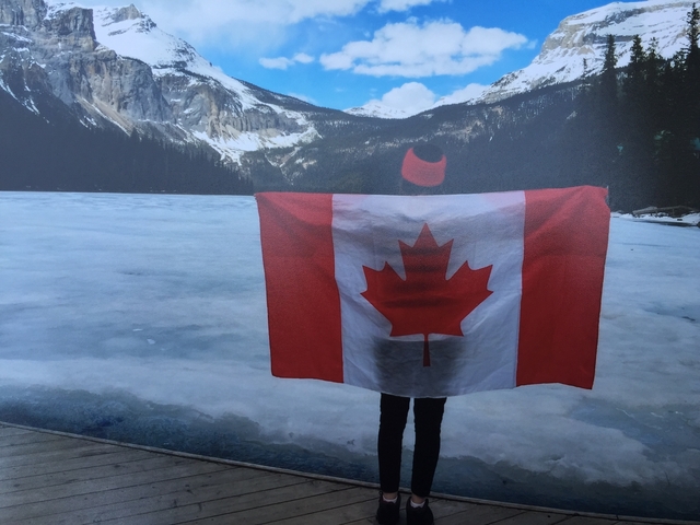       Person holding a Canadian flag with mountains and a frozen lake.
  