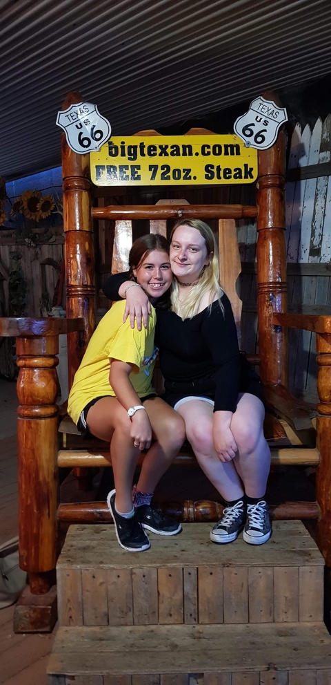 Two girls sitting on a large wooden chair in a dimly lit room.