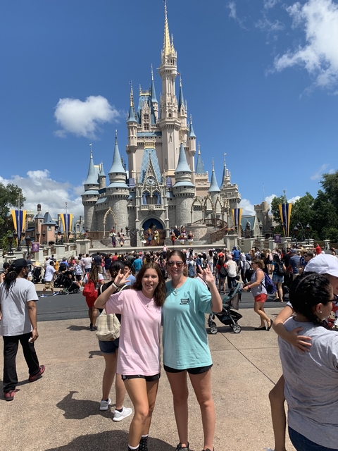 Two girls posing in front of a fairytale castle with a crowd.