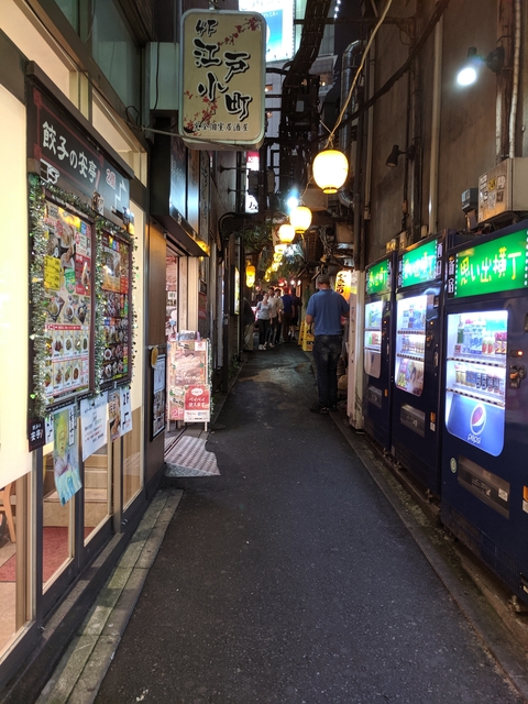       Narrow street with vending machines and hanging lanterns
  