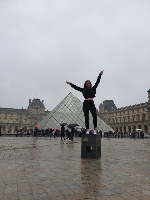 Person posing next to the glass pyramid of the Louvre.