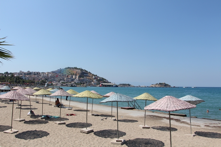 Beach with sun umbrellas and hillside town in the background.