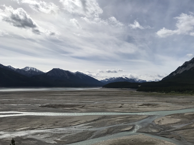 Mountain range with riverbed under cloudy sky.