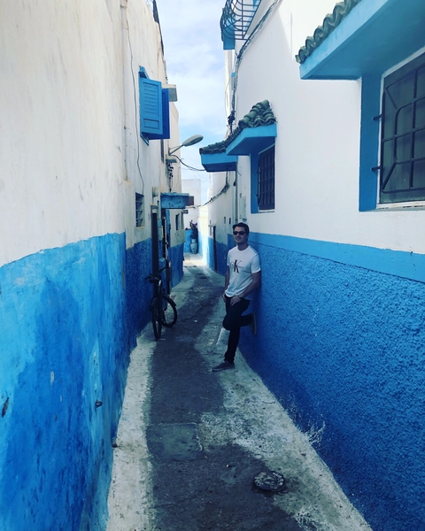       Person standing in narrow alley with blue and white walls.
  
