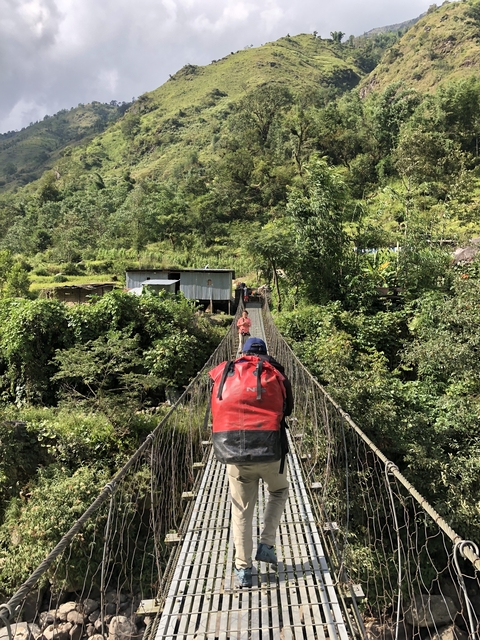 Person crossing a suspension bridge towards houses.