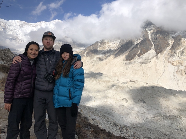 Three people posing in front of snowy mountains.