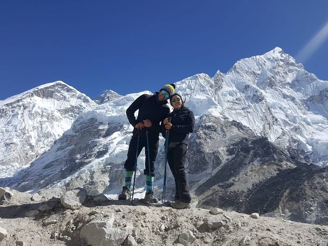       Two people with hiking poles in front of snowy mountains.
  