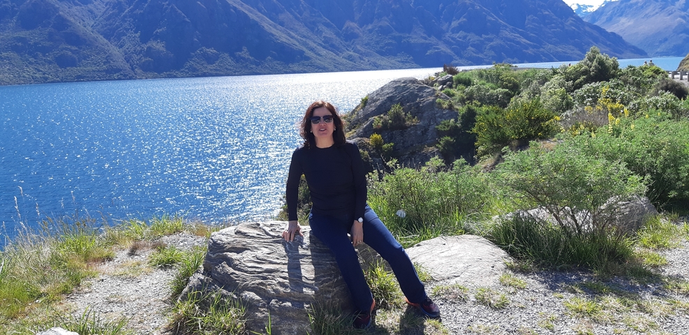 Person sitting on a rock near a lake with mountains in the background.