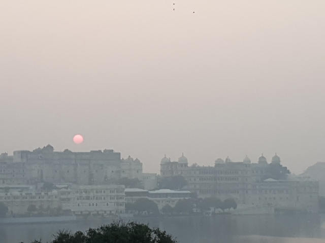 Hazy cityscape with the sun setting behind historic buildings.