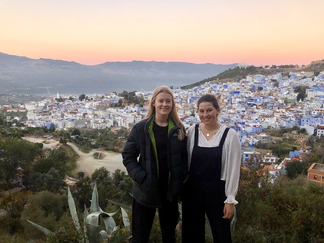       Two women posing in front of Chefchaouen's blue buildings.
  