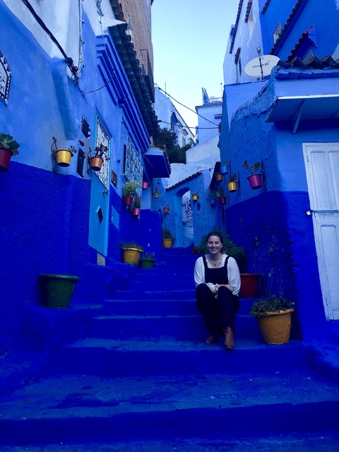       Woman sitting on blue steps of a narrow street in Chefchaouen.
  