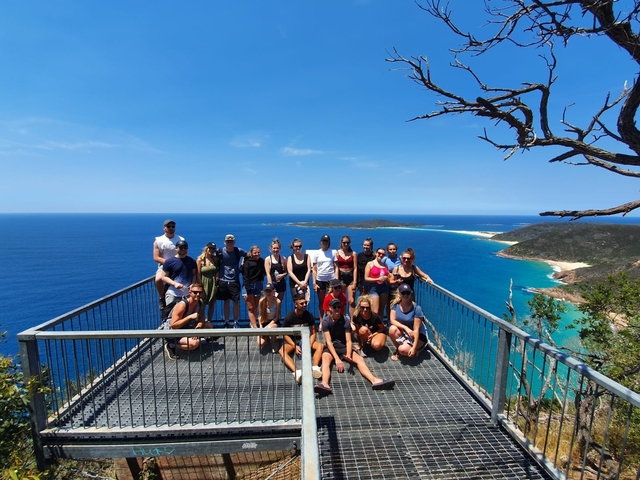       Large group on a viewing platform with ocean and islands visible.
  