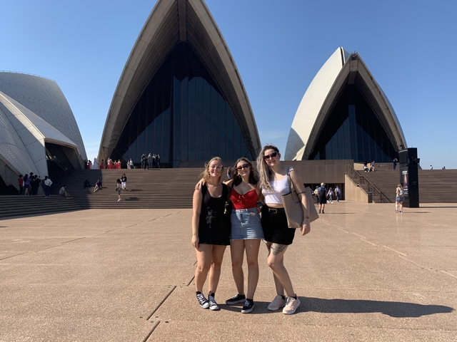 Three women posing in front of the Sydney Opera House.