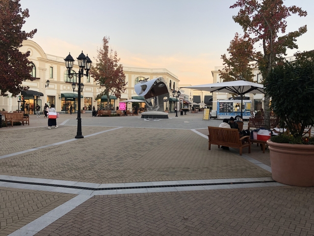 A quaint town square with people sitting on benches and a sculpture in the center.