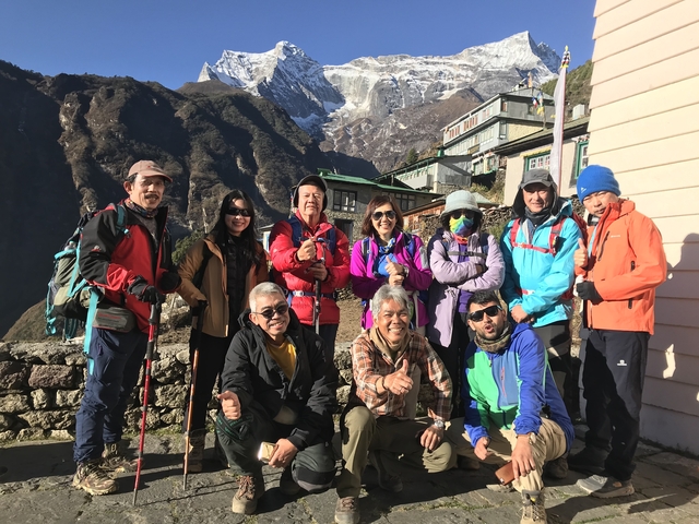 Group of hikers posing with a village and mountains in the backdrop.