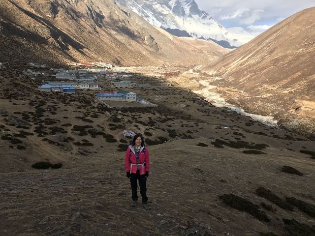 A woman posing on a hillside overlooking a village in a valley.