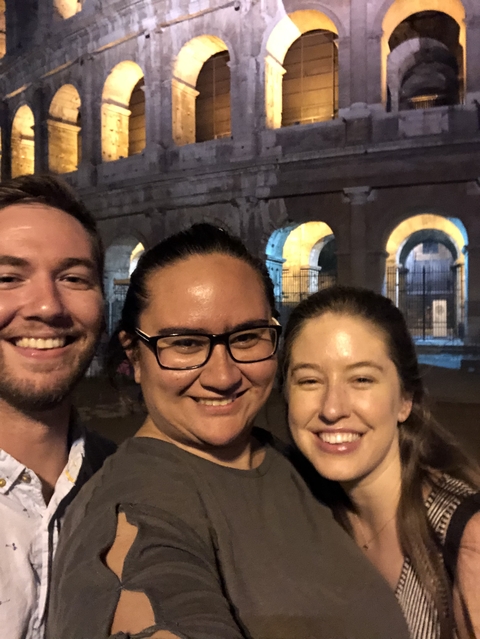 Three people smiling with an ancient structure in the background.