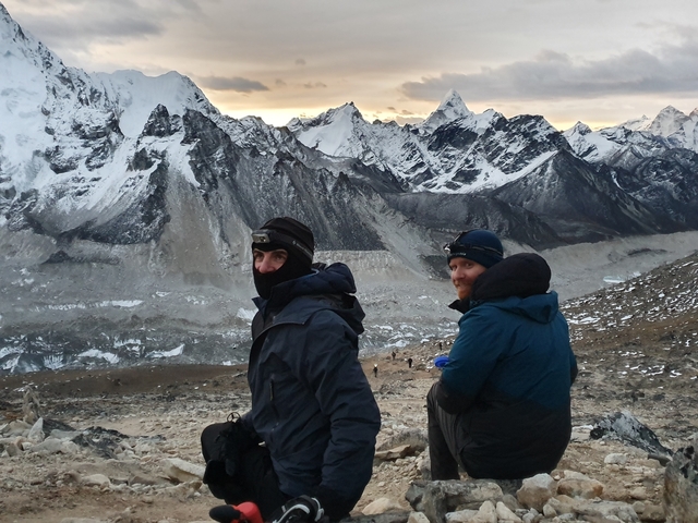 Two people in winter clothing in front of mountains.