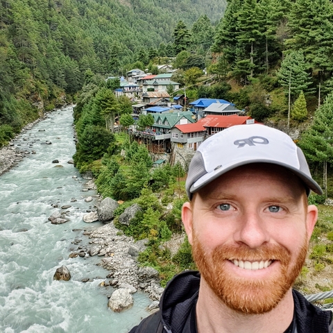 Smiling person in front of a river and colorful houses.