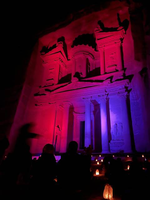 Illuminated ancient structure with people in the foreground.