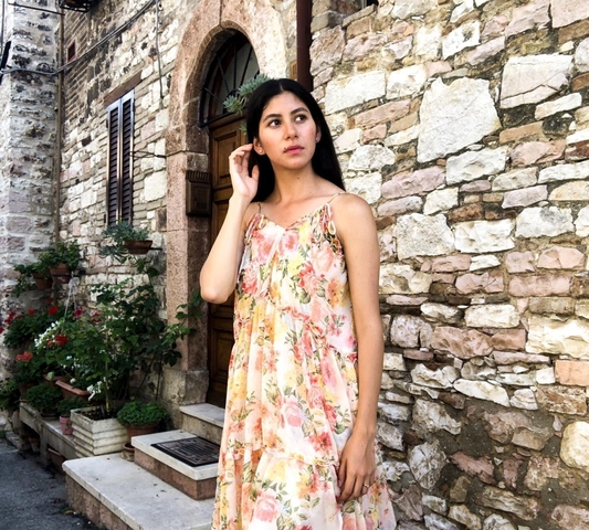 Woman standing by a stone wall with flowers in an urban setting.